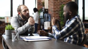 African american recruiter speaking with bearded man, discussing possible job opportunities. Black manager with pen in hand, advising male candidate about company internal regulations during interview